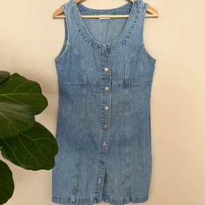 Ärmlös denimklänning från Sinclair by KappAhl - Säljer en snygg ärmlös denimklänning från Sinclair by Kappahl i storlek 40. Klänningen har knappar framtill och en klassisk blå denimlook. Figurnära passform och perfekt att styla upp med ex. vit t-shirt under.