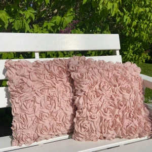 Rosa kuddfodral med rosmönster - Två dekorativa kuddfodral i ljusrosa med tredimensionellt rosmönster. Kuddfodralen är fyrkantiga och har en mjuk, romantisk look som passar perfekt i soffan eller på sängen. Materialet är textil med struktur av tygblommor.