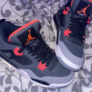 Jordan 4  - Säljer ett par gråa och svarta Nike Air Jordans med orange detaljer. Skorna har svart snörning, meshpaneler och en klassisk Jumpman-logga på plösen. Perfekta för dig som vill sticka ut med snygga sneakers, i bra skick. 