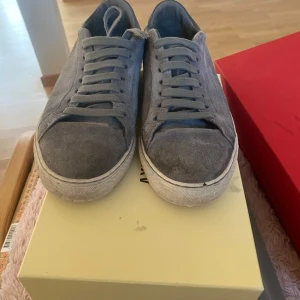 Gråa Clean 90 Suede sneakers från Axel Arigato - Säljer ett par stilrena gråa sneakers från Axel Arigato, modell Clean 90 Suede. Skorna är i mocka med snörning och har en vit platt sula. Perfekta för dig som gillar minimalistisk design och hög kvalitet.