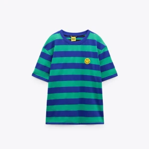 Randig t-shirt med smiley från Zara - Blå och grön randig t-shirt från Zara med en gul smiley på bröstet och en stor smiley på ryggen. T-shirten har rund hals och korta ärmar.