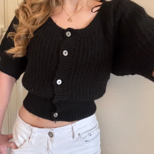 Svart stickad kofta med knappar - Säljer en svart stickad kofta med stora knappar framtill. Koftan har en croppad passform och lite lösare ärmar som slutar strax ovanför armbågen. Perfekt att styla till både jeans och kjol.