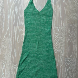 Grön stickad klänning med v-ringning - Snygg grön stickad klänning med v-ringad hals och smala axelband som korsas i ryggen. Klänningen har en tight passform och är perfekt för dig som gillar en enkel men trendig stil.