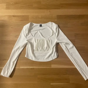 Vit ribbad topp med rynkade detaljer från SHEIN - Säljer en vit långärmad topp från SHEIN med ribbad struktur och rynkade detaljer framtill. Toppen har en rundad urringning och sitter figurnära. Perfekt att styla med jeans eller kjol.