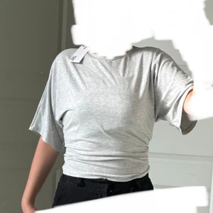 Tröja - Säljer en ljusgrå t-shirt som är tajt i midjan med korta ärmar och rund halsringning. Toppen har en enkel och stilren design i mjukt material, perfekt till vardags. Passar dig som gillar en avslappnad och trendig look. Lappen sitter kvar så den är aldrig använd.