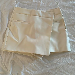 Kjol/shorts - Säljer en vanilj vit omlottkjol med shorts under, perfekt för en trendig och bekväm look. Kjolen har en stilren design med dolda fickor fram och dragkedja i sidan. Passar dig som gillar minimalistisk stil och vill ha något som sticker ut lite extra. Skicka om ni har frågor eller vill du hur plagget sitter på💕