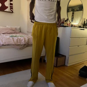 Gula träningsbyxor med svarta ränder - Säljer ett par gula träningsbyxor med svarta ränder längs sidorna. Byxorna har elastisk midja och raka ben. 