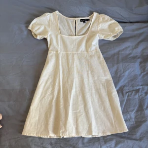 Vit klänning med puffärm från Motel Rocks - Söt vit klänning från Motel med korta puffärmar . Klänningen har en lätt utställd kjol och stängs med dragkedja i ryggen. Tillverkad i ett linneliknande material som känns luftigt och somrigt. Perfekt för studenten, avslutningen eller sommaren 💐🫶