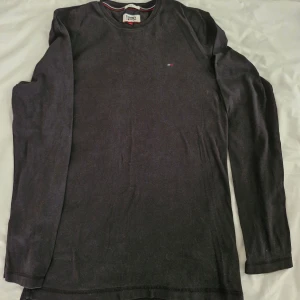 Marinblå långärmad tröja från Tommy Hilfiger Jeans - Marinblå långärmad tröja från Tommy Jeans i slim fit-modell. Tröjan har en liten broderad logga på bröstet och är tillverkad i mjukt material. Perfekt för en stilren och enkel look.