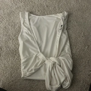 Vit topp med öppen rygg och knyte - Säljer en vit snygg topp med öppen rygg och knyte. Toppen är ärmlös och har en stilren design som passar till många olika outfits. Perfekt för dig som gillar enkla och snygga plagg.
