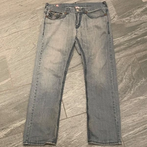 Ljusblå jeans från True Religion - Säljer ett par ljusblå jeans från True Religion med klassiska kontrastsömmar och snygga bakfickor med broderad logga. Jeansen har raka ben och silverfärgade knappar med märkets namn. Model ”JOEY SUPER T”.