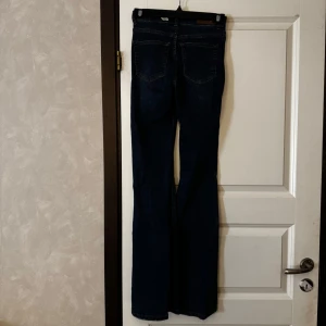 Mörkblå bootcut jeans  - Säljer ett par mörkblå jeans med klassisk bootcut-passform. Jeansen har fem fickor, synliga sömmar och normalhög midja. Perfekta för dig som gillar en tidlös jeansstil.