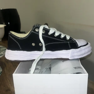 Svarta sneakers från Mihara Yasuhiro - Säljer ett par svarta Mihara Yasuhiro sneakers med vit, vågig sula och vita snören. Skorna har tydliga kontrastsömmar och en unik, chunky design. Perfekta för dig som vill sticka ut med din stil.