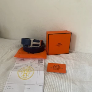 Blått skärp med silverfärgat H-spänne - Säljer ett stilrent blått bälte med ett stort H-format spänne i silver. Bältet har vit kontrastsöm längs kanterna och är gjort i skinn. Perfekt accessoar för att lyfta din outfit. Kvitto och allt hör av er vid intresse ! Helt nytt