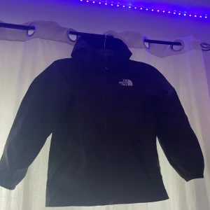   The North Face jacka  - Säljer en svart vindjacka från The North Face med huva och dragkedja framtill. Jackan har meshfoder på insidan och logga på bröstet. Perfekt för blåsiga dagar och enkel att matcha med olika outfits. Säljer den pågrund den passar inte mig längre 