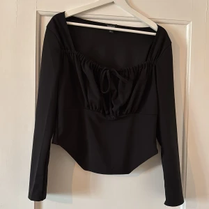 Svart långärmad topp med knyt från Boohoo - Säljer en svart långärmad topp från Boohoo med snygg knytning framtill och lätt v-ringad hals. Toppen har en figurnära passform och är perfekt för att lyfta en outfit.