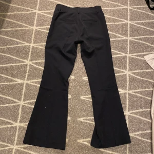 Svarta bootcut kostymbyxor RYVLS - Svarta kostymbyxor från RYVLS (kidsbrandstore) i klassisk bootcut-modell. Byxorna har hög midja, bälteshällor och två fickor, Snyggt skräddad passform och stilren look, perfekta till en dressad outfit. Provat 1 gång