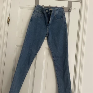 Levi's 721 High Rise Skinny Jeans - Säljer ett par klassiska blå Levi's 721 High Rise Skinny jeans i storlek 26. De är högmidjade med skinny fit och har fem fickor samt dragkedja och knapp framtill. Perfekta jeans för dig som gillar en tight och stilren look.