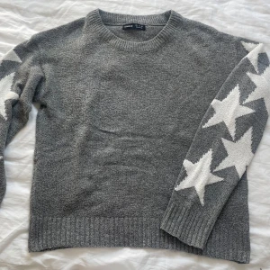 Grå stickad tröja med stjärnor Shein - Grå stickad tröja från Shein med vita stjärnor längs ena ärmen. Rund halsringning och ribbade muddar vid ärmslut och nederkant. Perfekt för dig som gillar en chill och trendig look med lite extra detaljer.