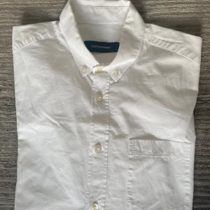 Vit skjorta från Peak Performance - Klassisk vit skjorta från Peak Performance i bomull. Skjortan har lång ärm, bröstficka och knappar hela vägen framtill. Snygg button down-krage och stilren design som funkar till allt. Perfekt för dig som gillar en clean och enkel look.