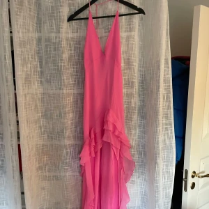 Rosa långklänning med volanger - Helt ny klänning med prislapp kvar! Supersnygg rosa långklänning med djup v-ringning och tunna axelband. Klänningen har flera lager volanger framtill som ger en riktigt cool och romantisk look. Perfekt för dig som vill sticka ut och känna dig extra fin. Materialet är lätt och flowy💕💕
