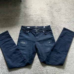 Mörkblå slim jeans Jack & Jones - Säljer ett par mörkblå slim jeans från Jack & Jones med slitna detaljer på benen. Man kan även byta storlek i midijan i jeansen med ett spännband i jeansen!Det står att de 158cm men jag är 170 och dom är nästan för små för mig! Dom passar om man är 168 och under! Dom är i väldigt bra skick och anvät fåtal gånger! Hör av er vid frågor!