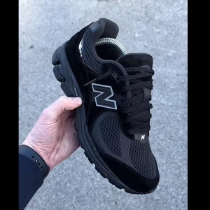 New Balance 2002R Mesh Black Metallic - Snygga New Balance 2002R sneakers i helsvart mesh och mocka med metallic-detaljer. Skorna har en chunky sula, klassisk N-logga på sidan och svarta skosnören. Perfekta för dig som gillar streetwear och vill ha en stilren look.