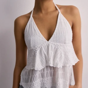 Vit halterneck topp med volang från Nelly - Halterneck topp från Nelly med volanger. Helt ny med prislapp kvar. Finns ej att köpa på hemsidan längre.