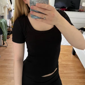 Svart ribbad kortärmad topp - En svart, ribbad topp med korta ärmar och rund halsringning. Sitter tight och har en enkel, stilren look som passar till det mesta. Perfekt för dig som gillar basic men ändå vill ha något som sitter snyggt. 