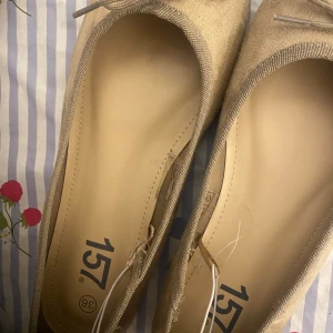Beige ballerinaskor med rosett - Snygga beige ballerinaskor från 157 med rund tå och söt rosettdetalj framtill. Skorna har en mjuk ovandel i mockaliknande material och en klassisk platt sula. Perfekta för dig som gillar en stilren och enkel look.