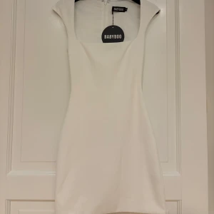 Vit kort klänning från Babyboo XS - Supersnygg vit kort klänning från Babyboo med fyrkantig urringning och figurnära passform. Klänningen är ärmlös och har dragkedja bak. Perfekt för dig som vill ha en clean och stilren look.