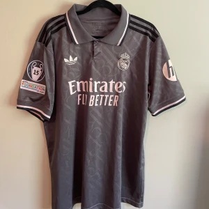 Real Madrid Valverde Adidas  - Snygg Real Madrid fotbollströja i mörkgrått med ljusa detaljer, Adidas logga och klubbmärke broderade på bröstet. Nummer 8 och Valverde på ryggen. Klassisk krage, korta ärmar och tryckta sponsorer. Tillverkad i lätt och ventilerande material.