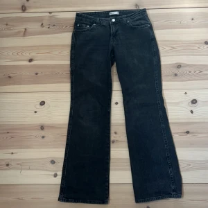 Svarta bootcut jeans från Gina Tricot - Snygga svarta bootcut jeans från Gina Tricot i klassisk femficksmodell. Jeansen har silverfärgade knappar och detaljer, samt bakfickor med lock och knapp. Materialet är robust denim i bomull. Perfekta för dig som gillar en tidlös och cool look.