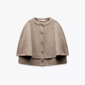 Beige stickad kofta från Zara - Superfin beige stickad kofta från Zara i cape-modell. Koftan har rund hals, knappar framtill och ribbade kanter. Perfekt lager-på-lager-plagg för höst och vinter. Snyggt oversized och riktigt mysig att bära. Jag bär vanligtvis S och M passa bra! Den blir pytte längre i längden bara, vilket jag bara tycker är najs