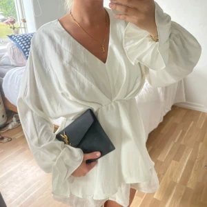 Vit omlottblus med vida ärmar🤍🤍 - Superfin vit omlottblus med djup v-ringning och långa, vida ärmar med volangkant. Blusen har en flowy passform och markerad midja som ger en snygg siluett. Perfekt att styla med smycken och en clutch för en chic look.🤍
