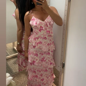 Lång blommig volangklänning från Vero Moda - Säljer en helt ny och superfin långklänning med rosa och vita blommor. Ordinarie pris 850kr. Slutsåld!  V-ringad framtill och lätt figursydd passform. Perfekt nu sommaren. Så skönt och svalt material🥰🌸🌿