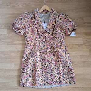 Blommig kortklänning från Glamorous - Superfin kortklänning från Glamorous med puffärmar, stor krage och blommigt mönster i rosa, gult och brunt/grönt på ljus botten. Klänningen har en figurnära passform och är perfekt för vår och sommar. Materialet känns som bomullsmix och ger en lyxig känsla. Aldrig använd och lapparna är fortfarande kvar💕