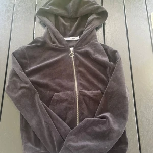 Svart velourhoodie från 157, XS - Mjuk och skön svart hoodie i velour från 157. Tröjan har huva, dragkedja med rund detalj och en stor ficka framtill. Perfekt för dig som gillar en chill och avslappnad stil.