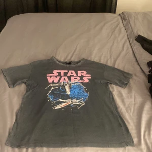 Star Wars t-shirt från Bershka - Cool svart t-shirt från Bershka med stort Star Wars-tryck i rosa och blått framtill. Motiv med X-wing och Dödsstjärnan ger en retro vibe. Klassisk passform med rund hals och korta ärmar. Perfekt för dig som älskar sci-fi och vill sticka ut.