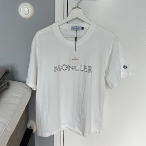 Vit Moncler t-shirt med logga - Vit t-shirt från Moncler i mjuk bomull med klassisk passform. Stor Moncler-logga tryckt på bröstet och diskret logomärke på ärmen. Perfekt basic med exklusiv känsla och snygg rund halsringning.