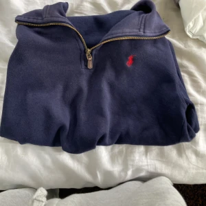 Mörkblå half zip från Polo Ralph Lauren - Mörkblå långärmad tröja från Polo Ralph Lauren med klassisk röd logga broderad på bröstet. Tröjan har en snygg half zip-dragkedja och är gjord i mjuk bomull. Perfekt för lager-på-lager och chill stil.
