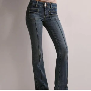Mörkblå jeans med fickdetaljer - Snygga mörkblå jeans med raka ben och markerade sömmar framtill. Byxorna har dubbla knappar i midjan. Jeansen är från Nelly och är i toppskick då dem endast används 1 gång