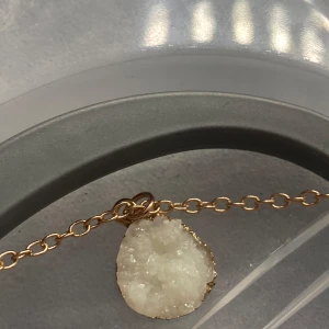 Halsband med vit kristallhänge - Unikt halsband med en kedja i guldton och ett rått, vitt kristallhänge. Hänget har en oregelbunden form och gnistrar snyggt i ljuset. Perfekt för dig som gillar naturliga stenar och vill ha något som sticker ut.
