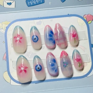 Handmålade rosa och blå lösnaglar - Säljer ett set med 10 handmålade lösnaglar i mandelform. Naglarna har unika motiv med blommor, hjärtan och mönster i rosa, blått och vitt på transparent bas. Perfekt för dig som vill ha en söt och färgglad.