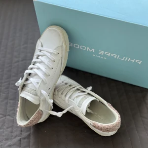 Vita Philippe Model sneakers med rosa detalj - Sprillans nya Philippe Model med klassisk låg profil, snörning och en rund tå. Skorna har en rosa stickad detalj baktill på hälen samt en silvrig logga på sidan. Strlk 39, DM för fler bilder😌 