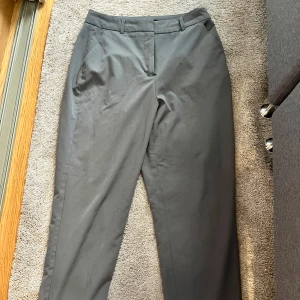 Grå kostymbyxor från Vero Moda - Snygga grå kostymbyxor från Vero Moda med klassisk rak passform och hällor för bälte. Byxorna har diskreta sidfickor och stängs med dragkedja och knapp. Perfekta för en clean och stilren look. De var tyvärr lite för stora på mig!