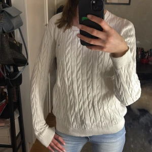 Vit kabelstickad tröja från Tommy Hilfiger - Säljer en vit kabelstickad tröja från Tommy Hilfiger som är köpt secondhand! Perfekt för en avslappnad och snygg look. Passar bra till jeans eller kjol! Går även att vika upp kanten för en kortare tröja som visad i bild 4&5🥰