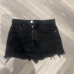 Svarta jeansshorts från Zara - Snygga svarta jeansshorts från Zara med hög midja och fransiga kanter. Shortsen har knappar framtill och klassiska femficksdetaljer. Perfekta för en cool och avslappnad stil.