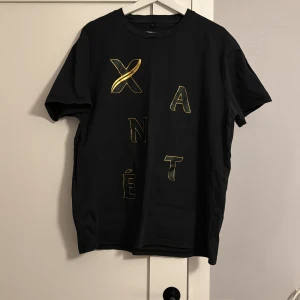Svart t-shirt med Xanté-tryck - Snygg svart t-shirt med guldtryck från Xanté. En sällsynt och limiterad Xante tröja från Åre! Använd en gång! Storlek large! Väldigt efterfrågad tröja! Börjar på ett högt belopp men självklart går det att diskutera pris vid snabb affär 