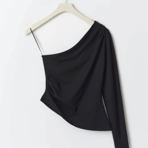 Svart oneshoulder topp - Snygg svart oneshoulder topp med en lång ärm och en smal axelrem. Perfekt för en stilren och modern look. Passar bra till både jeans och kjol. Storlek xs från Gina tricot, aldrig använd.